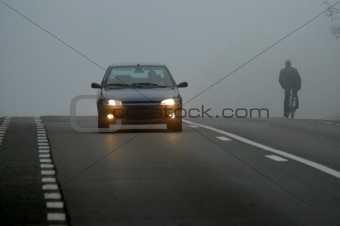 Car appearing through fog and cyclist riding in