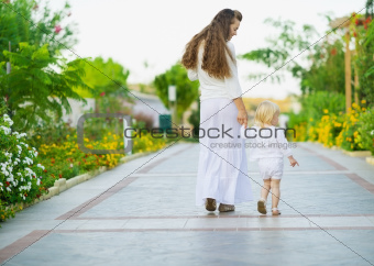 Mother and baby walking outdoors. Rear view