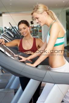 Woman Working With Female Personal Trainer On Running Machine In Gym