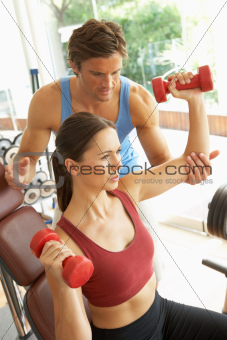 Young Woman Working With Weights In Gym With Personal Trainer