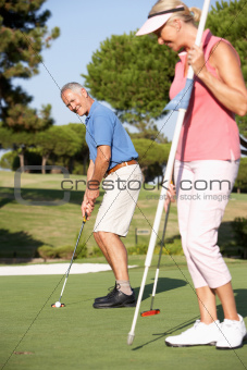 Senior Couple Golfing On Golf Course Lining Up Putt On Green