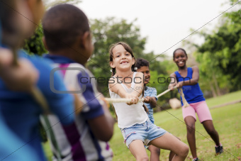 Happy school children playing tug of war with rope in park
