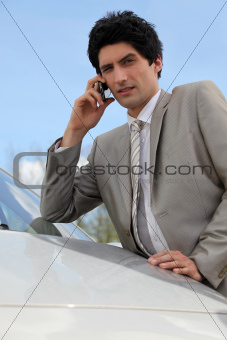 Annoyed businessman talking on his mobile phone by his car