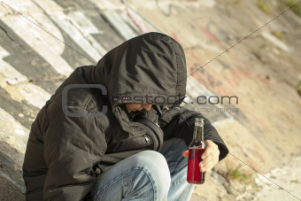 Boy with a bottle of hands sit under a bridge