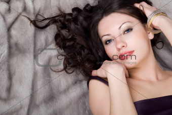 Sexy young woman lying on grey fur coat