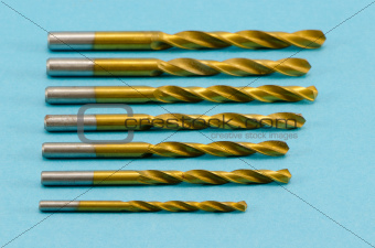 various size golden drill bits on blue 