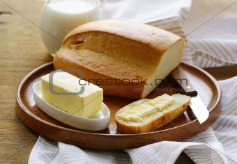 butter,  loaf of white bread and milk on wooden plate