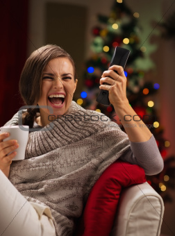 Excited young woman with cup of hot beverage looking TV