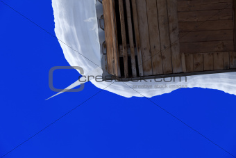 Snowdrift and big icicle on wooden roof