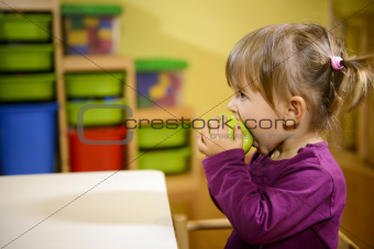 female child eating green apple in kindergarten