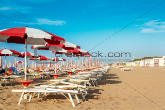 red and white umbrellas and sunlongers on the sandy beach