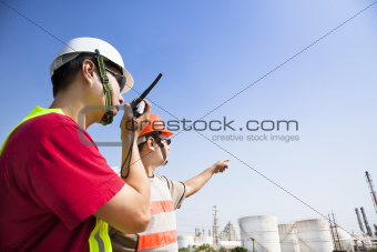 two refinery workers looking the large refinery background