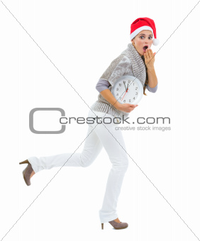 Shocked woman in Santa hat holding clock and running
