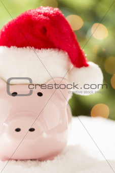 Pink Piggy Bank Wearing Red and White Santa Hat on Snowflakes with Abstract Green and Golden Background.