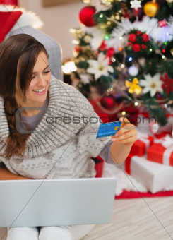 Smiling woman with laptop and credit card near Christmas tree