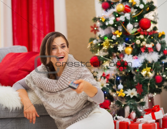 Surprised young woman watching TV near Christmas tree