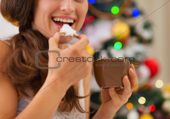 Closeup on young woman eating cookies with hot chocolate near Christmas tree