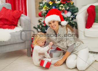 Baby sitting near mother and open Christmas present box