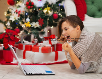 Happy woman with laptop near Christmas tree rejoicing success