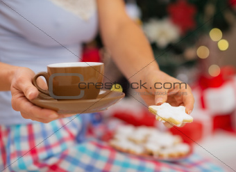 Closeup on woman in pajamas holding hot beverage and cookies in front of Christmas tree