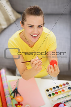 Smiling young woman drawing on Easter red egg