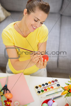 Happy young woman drawing on Easter red egg