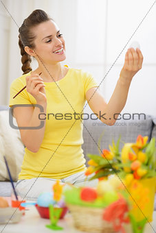 Young woman preparing for Easter and drawing on egg