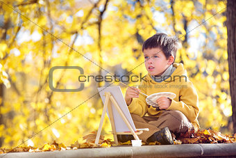 Cute little boy painting with brush outdoors in park on beautiful autumn day