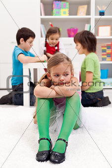Sad little girl sitting excluded by the other kids