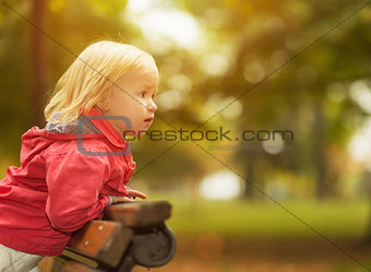 Baby leaning on bench and looking on copy space