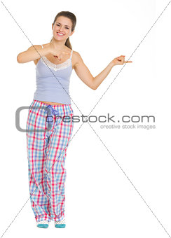 Full length portrait of young woman in pajamas pointing on copy 