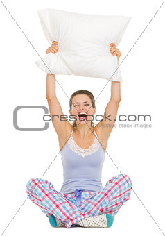 Cheerful young woman in pajamas sitting and holding pillow