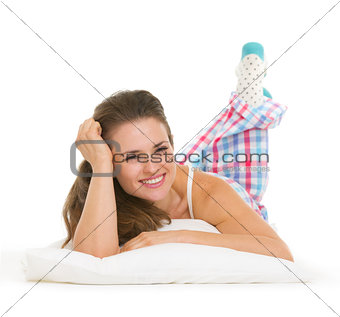 Smiling young woman in pajamas laying on pillow isolated on whit