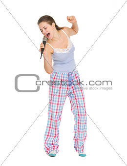 Full length portrait of young woman in pajamas singing in microp