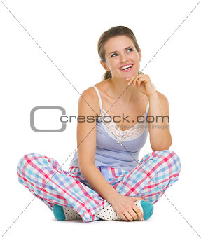 Thoughtful young woman in pajamas sitting on floor and looking o