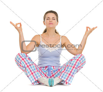 Happy young woman in pajamas sitting on floor and meditating