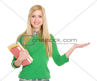 Smiling student girl with books showing something on palm