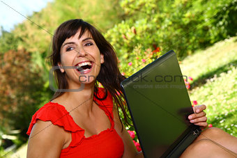 Happy woman with a computer laughing outside in the sunshine.