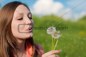 Young beautiful woman blowing on dandelion flower