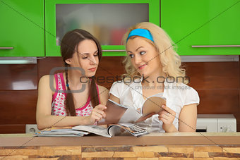 Two girlfriends with women's magazines on kitchen