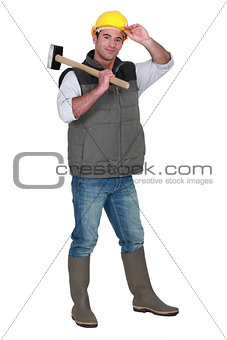Tradesman carrying a mallet and wearing a hard hat and rubber boots