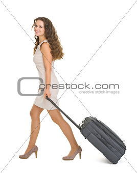 Happy young woman walking with wheels suitcase