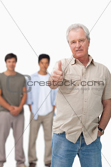 Senior man giving thumb up with young people behind him
