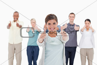 Close-up of a smiling woman giving the thumbs-up with people beh