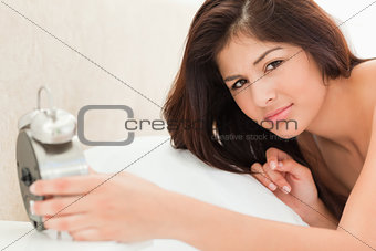 Woman is lying on a bed with a clock in her hand and is looking 