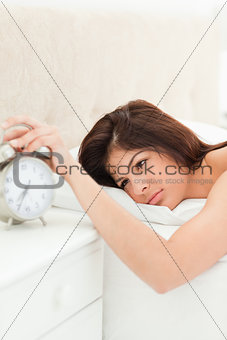 A woman lying on her bed, awake with her hand on the alarm clock