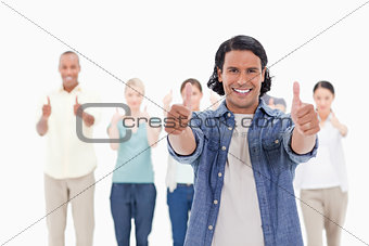 Close-up of a man smiling with his thumbs-up with people behind