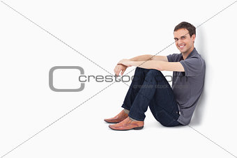 Man smiling while sitting against a wall 