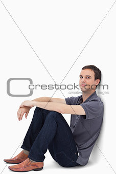 Close-up of a dark brown hair man sitting against a wall 