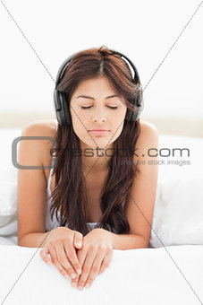 Woman at the edge of the bed listening to music with her eyes cl